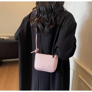 Close-up of pink litchi grain leather crossbody bag with logo on black coat