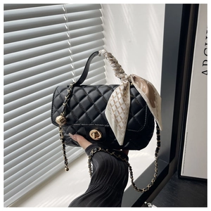 Detail of black quilted leather box bag with silk scarf handle and golden chain strap