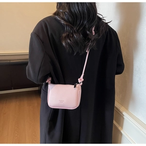 Detail of pink pebbled leather crossbody bag with adjustable knot strap and logo