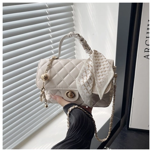 Detail of beige quilted bag with woven handle, gold ball charm, and silk scarf decor
