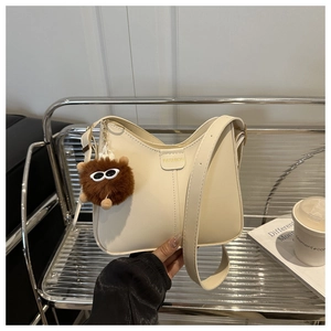 Detail of cream shoulder bag with FASHION text and brown plush pompom charm accent