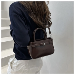 Gros plan d'un sac bandoulière en cuir verni marron foncé avec boucles argentées