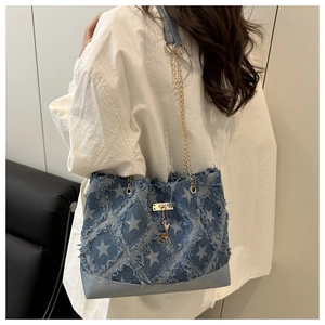 Détail d'un cabas en jean bleu avec étoiles blanches, bords effilochés et pendentif cerf