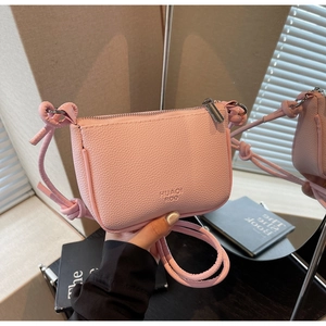 Close-up of light pink lychee leather handbag with silver zipper and knotted strap detail
