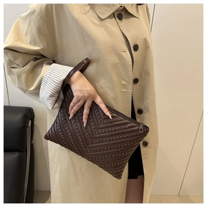 Detail of dark brown studded shoulder bag with V-shaped rivets held by a model