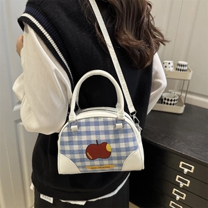 Blue and white checkered handbag with red apple print worn by a model in a home setting