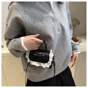 Close-up of black mini bag with white lace trim and bow on a model's shoulder