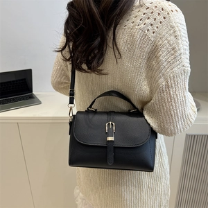 Sac bandoulière noir minimaliste avec boucle dorée sur fond de bureau épuré