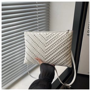 Detail of white quilted bag with V-shaped stitching and dark metallic studs in hand
