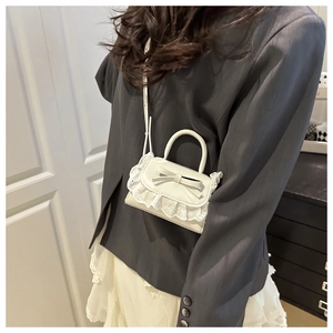 Detail of white mini crossbody bag with delicate lace trim and sweet bow accent