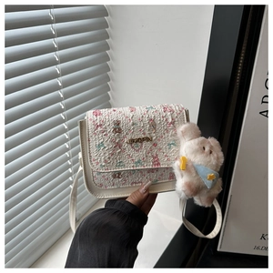 Close-up of white embossed crossbody bag with pink floral patterns and plush rabbit charm