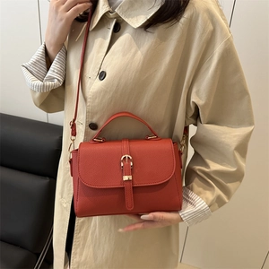 Petit sac carré rouge en cuir avec boucle dorée porté sur un trench-coat élégant