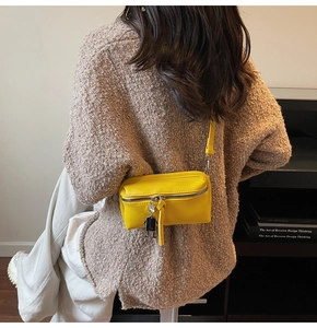 Close-up of bright yellow rectangular crossbody bag with metal zipper and charm detail