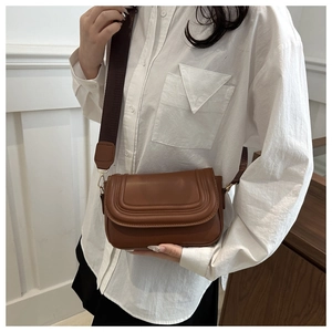 Dettaglio borsa a sella in pelle marrone con linee goffrate e ampia tracolla in nylon marrone