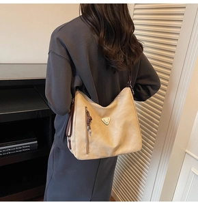 Detail of beige hobo tote bag featuring a triangle metal logo and side zipper