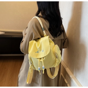 Detailed view of yellow nylon backpack featuring blue cursive embroidery and colorful drawstrings