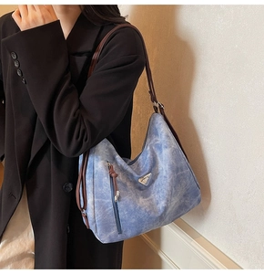 Détail du sac hobo en denim bleu avec anses en cuir marron et logo métallique