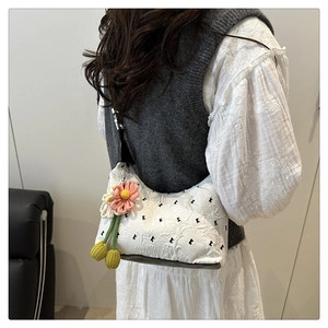 Detail of white pleated handbag featuring black K embroidery and a colorful flower charm
