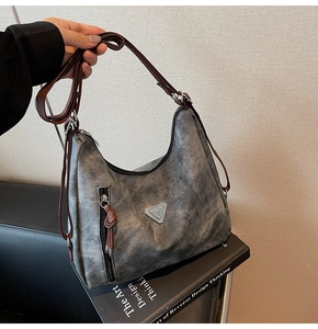 Détail d'un sac hobo gris vieilli avec bandoulière réglable marron et logo en métal