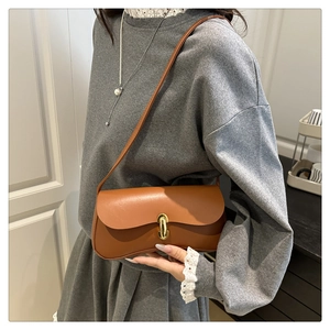 Detail of a brown leather shoulder bag with a gold capsule lock on a model's arm