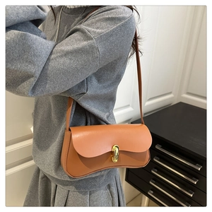 Detail of a brown leather underarm bag with a golden buckle on a grey knit outfit