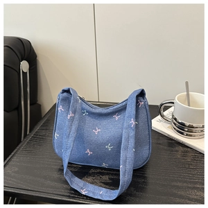Detail of blue denim hobo bag featuring pink and green embroidered bow patterns