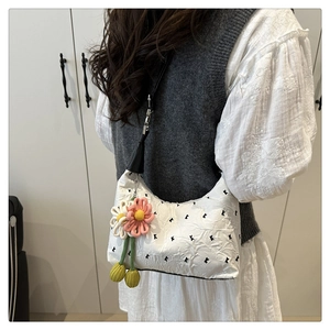 Detail of white pleated shoulder bag featuring black floral embroidery and floral charm