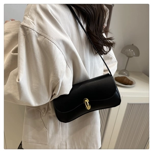 Detail view of a black leather handbag with a gold metal lock and shoulder strap on a model