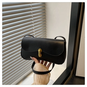 Close-up of minimalist black baguette bag with gold buckle and smooth leather texture