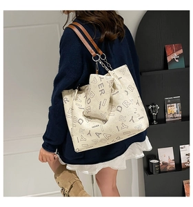 Detail of cream tote bag featuring letter print with chain strap and matching pouch