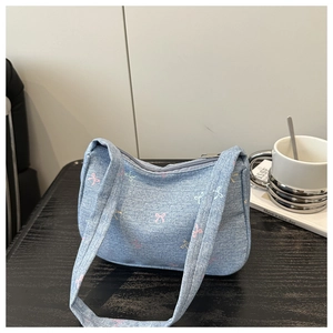 Blue denim underarm bag with colorful bow embroidery placed on a cafe table next to a coffee cup