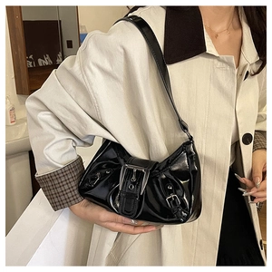 Detail of a shiny black faux leather shoulder bag with metallic buckle and Y2K aesthetic