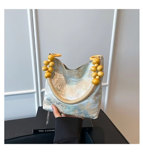 Detailed embroidery of gold landscapes on a light blue brocade bag with wooden bead handle