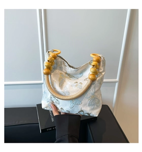 Detailed embroidery of blue butterflies on a satin shoulder bag with wooden bead handles