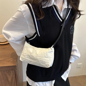 Minimalist white pleated crossbody bag with a slim black strap worn by a female model