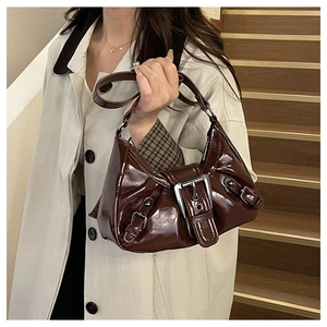 Detail of dark reddish-brown patent leather shoulder bag with glossy finish and silver buckle