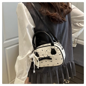 Detail of white pleated crossbody bag with black bow and pearl lace charm