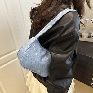 Blue denim shoulder bag featuring colorful bow patterns and trendy crescent silhouette