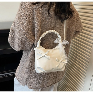 Detail view of white soft leather bucket bag with 3D bow and lace charm on shoulder strap