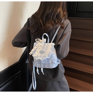 Detail view of a light blue plaid backpack with a lace bow on a wooden staircase