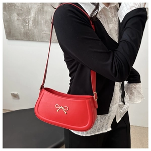 Detail of red leather shoulder bag featuring a gold metallic bow buckle and smooth texture