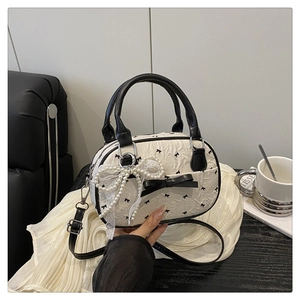 Detail of cream Boston bag with black bow patterns and elegant pearl bow pendant charm