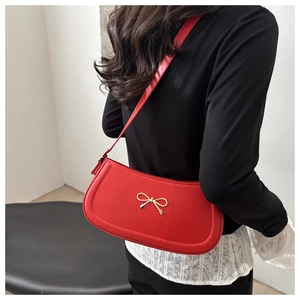 Detail of red underarm bag featuring a golden bow metal buckle on a shoulder strap