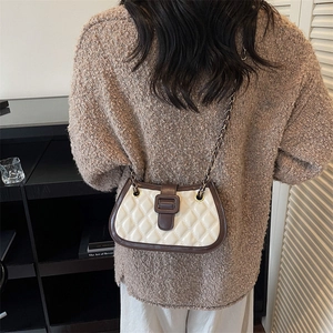 Quilted cream crossbody bag with brown trim and chain strap shown on model's shoulder
