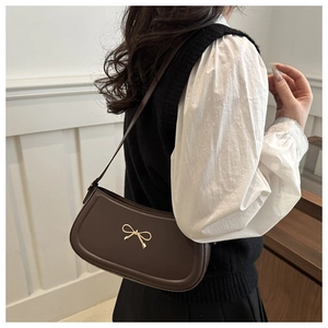Close-up of a dark brown crescent underarm bag featuring a golden metallic bow detail