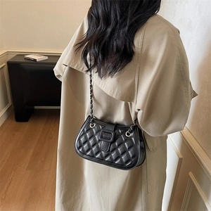 Classic black quilted crossbody bag with chain strap and square buckle on khaki trench coat