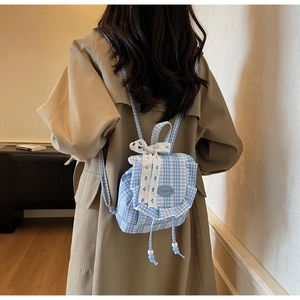 Detail of blue gingham mini backpack with lace trim and bow on khaki trench coat