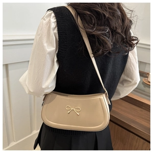 Detail of elegant beige baguette shoulder bag with golden bow buckle on a female model