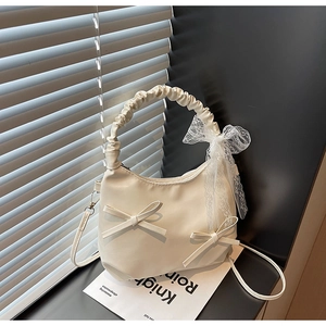 Detail of cream hobo bag featuring decorative bows and delicate white lace pendant