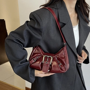 Chic burgundy patent leather shoulder bag with metallic buckle worn by a model